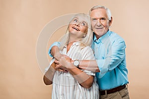 happy pensioner hugging cheerful retired wife on beige.