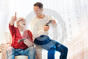 Happy pensioner pointing to the screen while playing video games with son