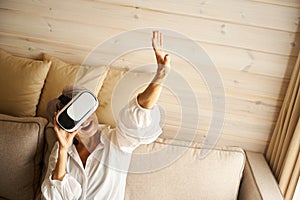 Happy pensioner sits on sofa in room playing virtual game