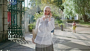 Happy pensioner speaking cellphone in city garden. Smiling senior enjoying call