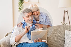 Happy pensioners using tablet, relaxing on rug