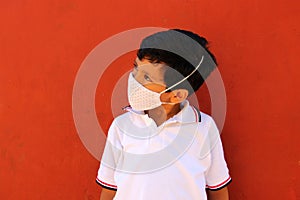 Happy and pensive Latino 8 year old boy wearing white school uniform shirt and face mask for protection in the Covid-19 pandemic a