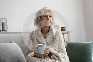 Happy pensive senior 60s woman wrapped in woolen plaid