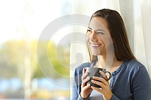 Happy pensive woman looks at side beside a window