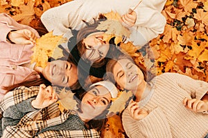 Happy people. Autumn portrait. Happy young women students playing with leaves, smiling while lying on ground in park