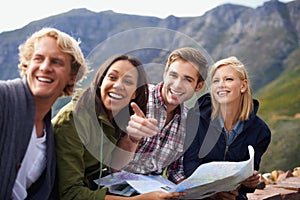 Happy people, friends and pointing with map for travel, location or destination on mountain in nature. Young group with