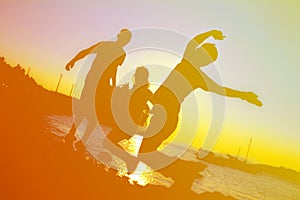 Happy people jumping on the beach while sunset, silhouette image