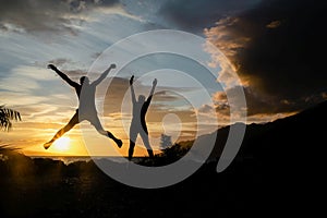 Happy people jumping over sunset, concept having fun and joy. Two silhouettes and a beautiful sunset