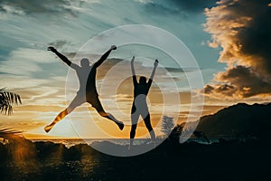 Happy people jumping over sunset, concept having fun and joy. Two silhouettes and a beautiful sunset