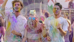 Happy people moving to music at Holi festival, friends covered in colored paint