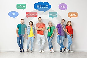 Happy people posing near light wall and illustration of speech bubbles with word Hello written in different languages