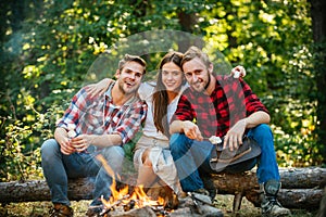 Happy people sitting around campfire. Friends roasting hotdogs on sticks at bonfire and having fun at camp fire. Summer