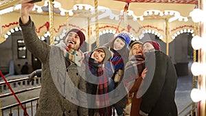 Happy people taking selfie photo on smartphone camera at New Year winter fair amusement park. Smiling friends have fun