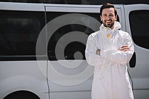 happy pest control worker in uniform standing with crossed arms near car