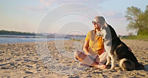 Happy pet owner relaxing and hugging her dog on the beach in summer