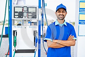 Happy petrol pump worker standing with crossed arms by looking camera at gas filling station - concept of successful