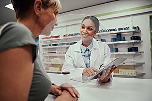 Happy pharmacist talking to customer while holding and showing screen on digital tablet while guiding on medicine
