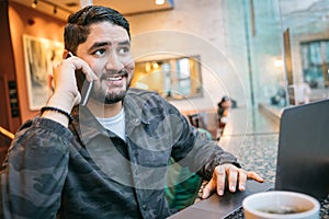 Happy phone chatting man in cafe with computer. Freelancer employed out office workplace