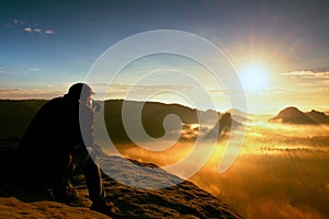 Happy photo enthusiast is enjoying fantastic miracle of nature on cliff on rock. Dreamy fogy landscape bellow.