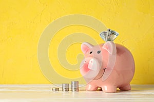 Happy piggy bank with money on white table against color background, space for text