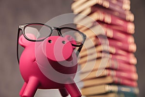 Happy piggy bank wearing glasses looks up near books