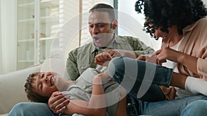 Happy playful African American mother father tickle little boy adopted son funny multiracial parents and kid playing