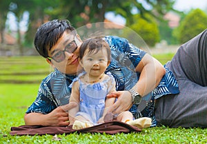 Happy playful Asian Japanese man as loving father enjoying sweet and beautiful baby girl daughter sitting together playing on