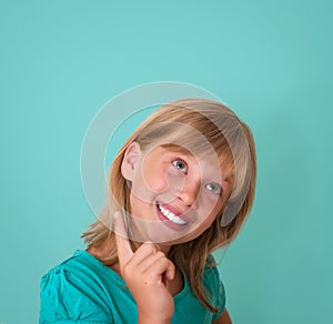 Happy playful child smiling happy and joyful on turquoise background. Thinking beautiful girl looking to the side