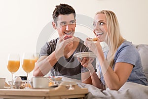 Happy playful couple enjoying breakfast in bed