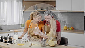 Happy playful family of three making flour exposure, clapping hands with powder and laughing, having fun at kitchen