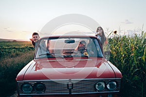 Happy playful family traveling together by the car, beautiful young mom driving and her children got out the car windows