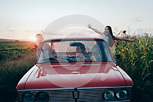 Happy playful family traveling together by the car, beautiful young mom driving and her children got out the car windows