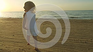 Happy playful little girl in white dress running on the beach sand