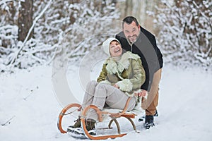 Happy playful mature family couple sledding in winter park, laughing and having fun together