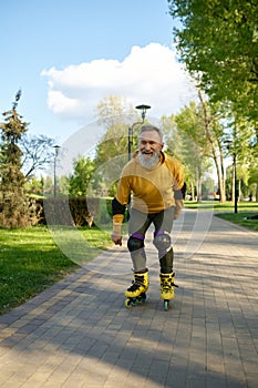 Happy playful mature man rollerskating on pathway in city park