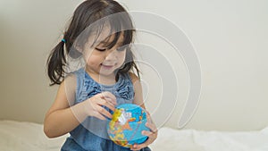 Happy playful toddler looking at globe ball on bed in bedroom at home