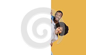 Happy and playful young couple peeking out with beaming smiles, the man holding a sign