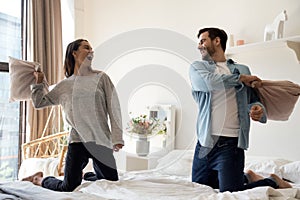 Happy playful young romantic couple playing pillow fight on bed