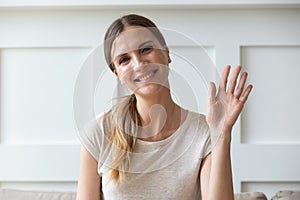 Happy pleasant young woman looking at camera, waving hello.