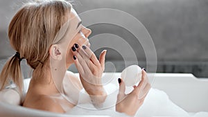 Happy pleased girl enjoying applying face cream to smooth pure face skin close-up in bathroom
