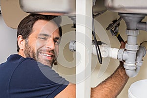Happy plumber fixing under the sink
