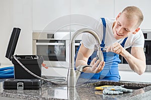 Happy plumber repairing kitchen`s faucet