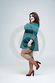 Happy plus size fashion model in green dress, fat woman on gray background, body positive concept