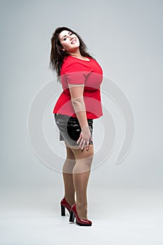 Happy plus size fashion model in red blouse and black skirt, fat woman on gray background, body positive concept
