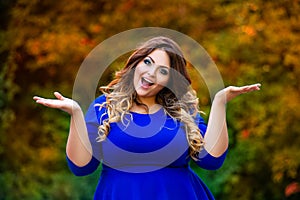 Happy plus size model in blue dress outdoors, fat woman in autumn park among yellow leaves