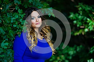 Happy plus size model in blue dress outdoors, fat woman in autumn park among yellow leaves