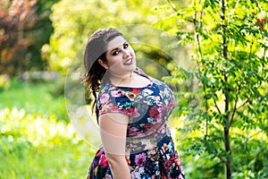 Happy plus size model in floral dress outdoors, beautiful fat woman in nature