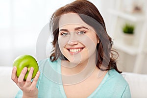 Happy plus size woman eating green apple at home