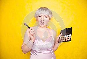 Happy plus size woman having fun with make-up palette set and brush. Professional multicolor eyeshadow face corrector