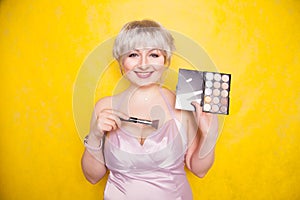 Happy plus size woman having fun with make-up palette set and brush. Professional multicolor eyeshadow face corrector